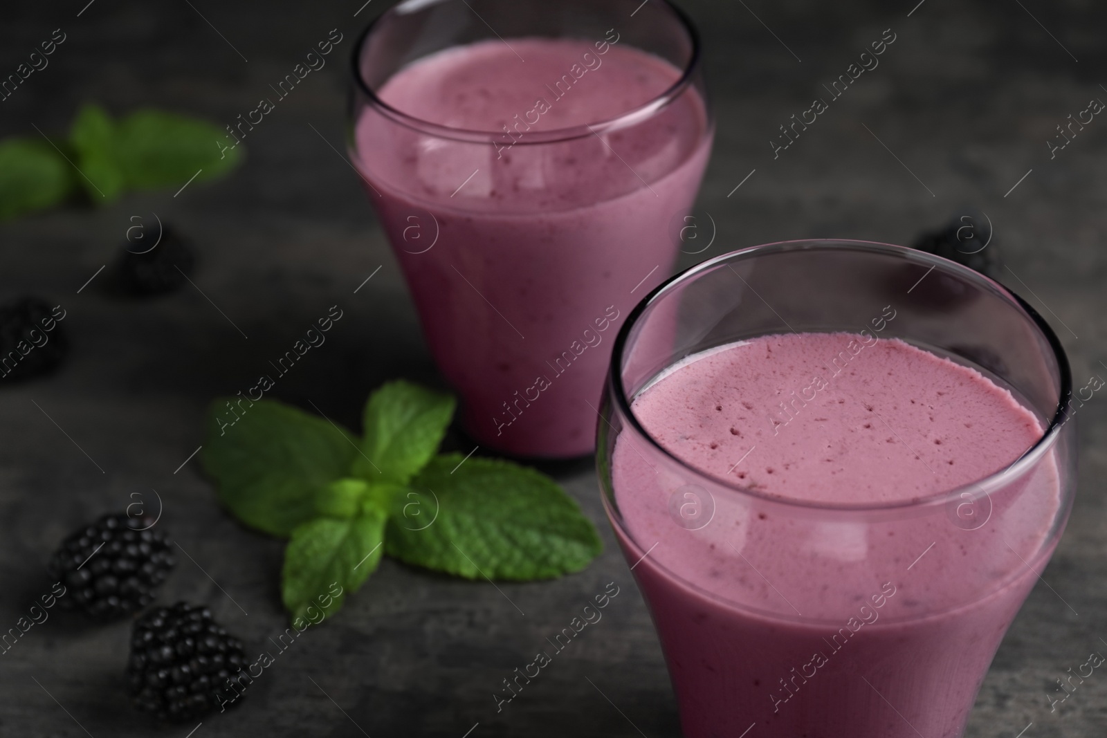 Photo of Glasses with blackberry yogurt smoothies on grey table, closeup