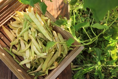 Photo of Crate with fresh green beans on wooden table in garden, top view