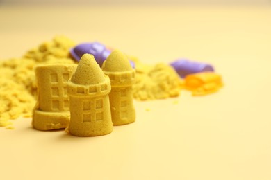 Photo of Castle figures made of yellow kinetic sand on beige background, closeup. Space for text