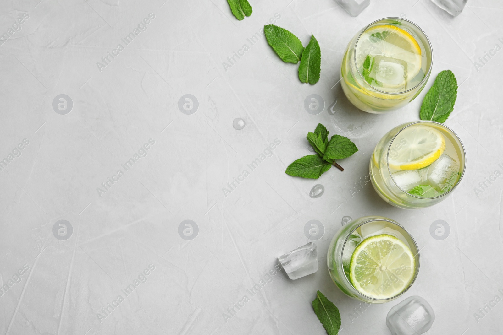 Photo of Flat lay composition with glasses of refreshing lemonade on grey background, space for text. Summer drink