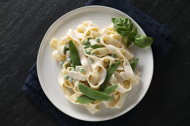 Photo of Delicious pasta with green peas and creamy sauce on black table, top view