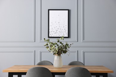 Photo of Vase with eucalyptus branches on wooden table in stylish dining room