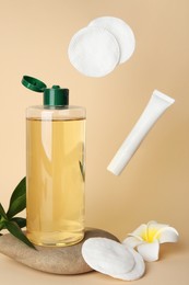 Photo of Tube of cream and cotton pads flying near bottle of micellar water on beige background