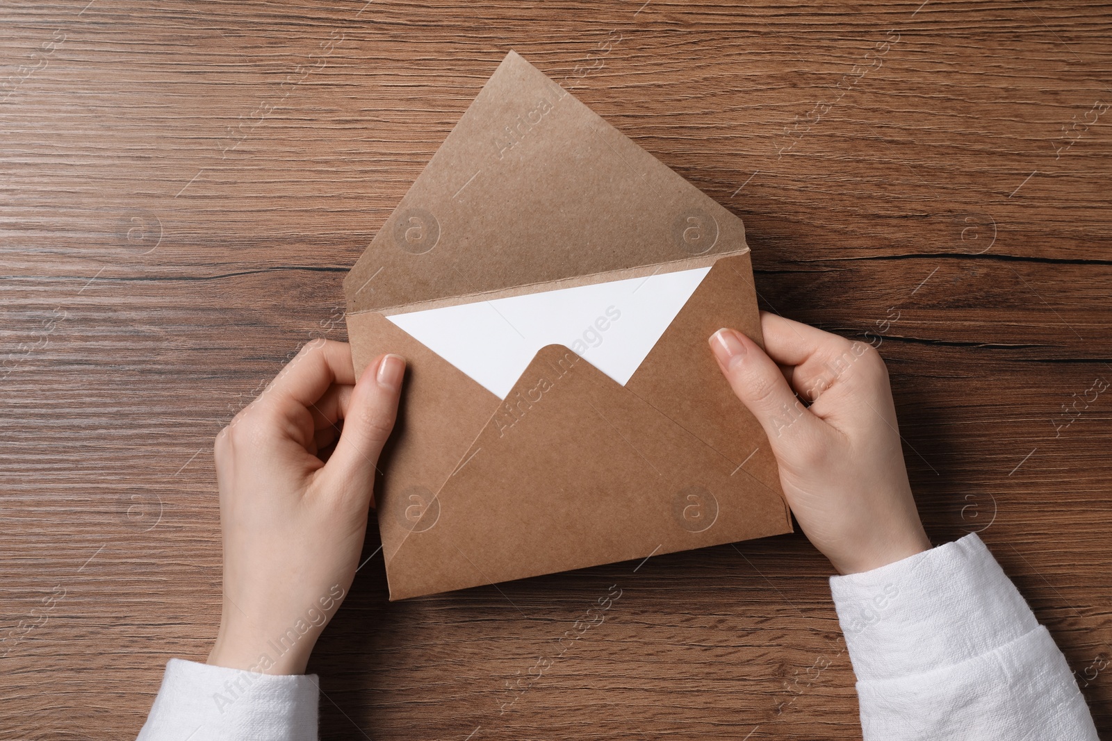 Photo of Woman holding letter envelope with card at wooden table, top view