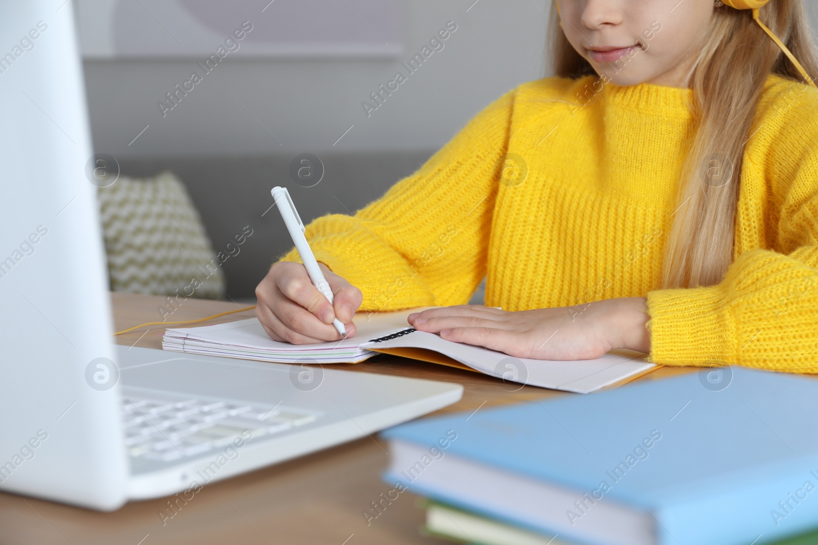 Photo of Cute little girl with modern laptop studying online at home, closeup. E-learning