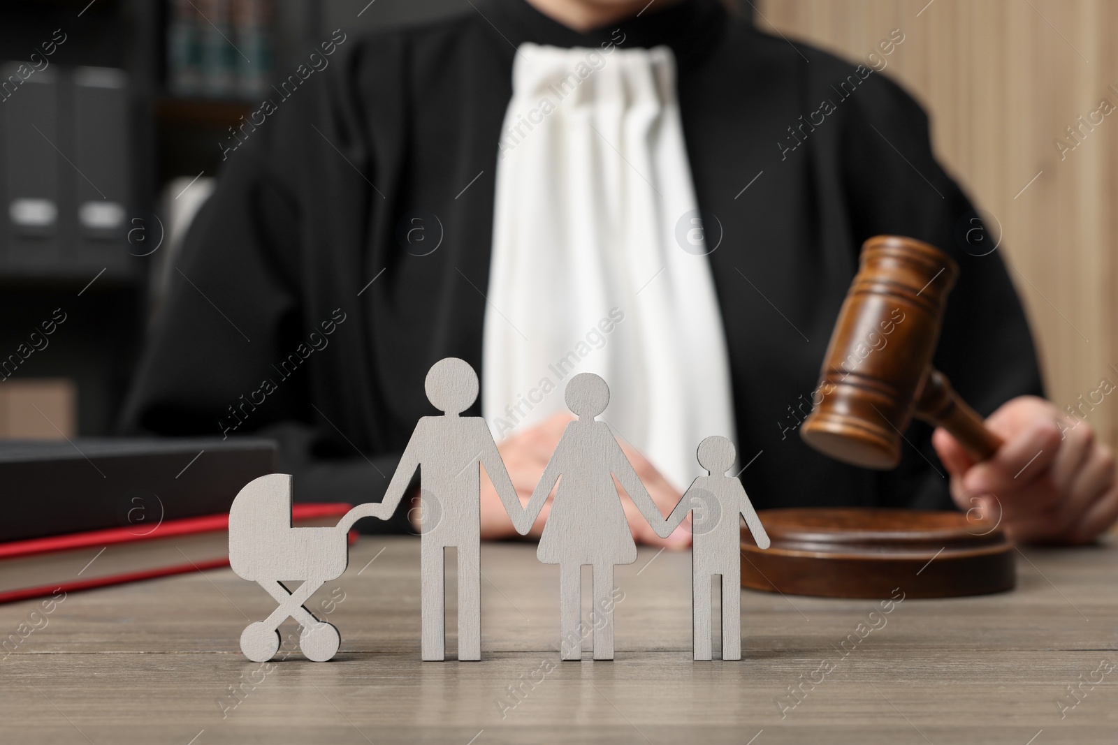 Photo of Family law. Judge with gavel sitting at wooden table, focus on figure of parents and children