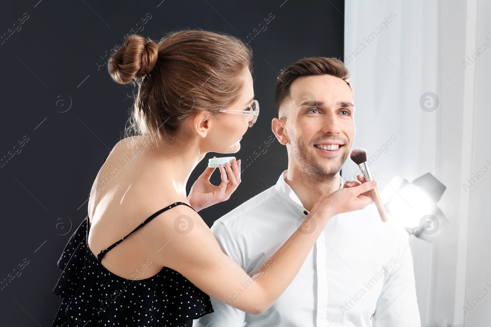 Photo of Professional makeup artist working with  young man in photo studio