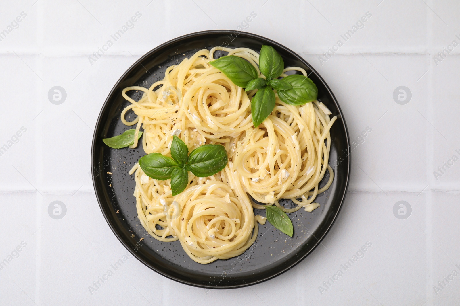 Photo of Delicious pasta with brie cheese and basil leaves on white tiled table, top view