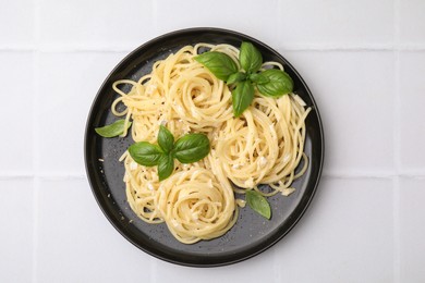 Delicious pasta with brie cheese and basil leaves on white tiled table, top view