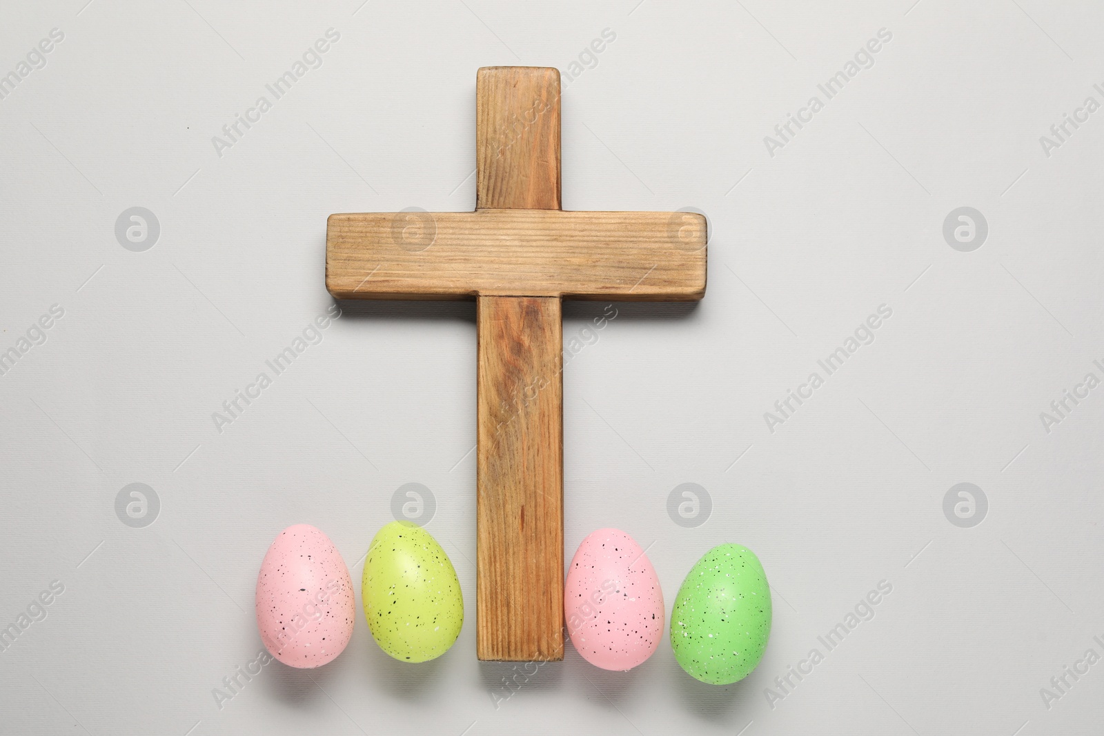 Photo of Wooden cross and painted Easter eggs on light grey background, flat lay