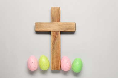 Wooden cross and painted Easter eggs on light grey background, flat lay