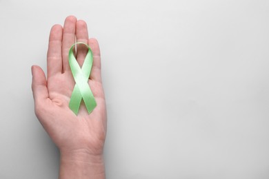 World Mental Health Day. Woman holding green ribbon on color background, top view with space for text