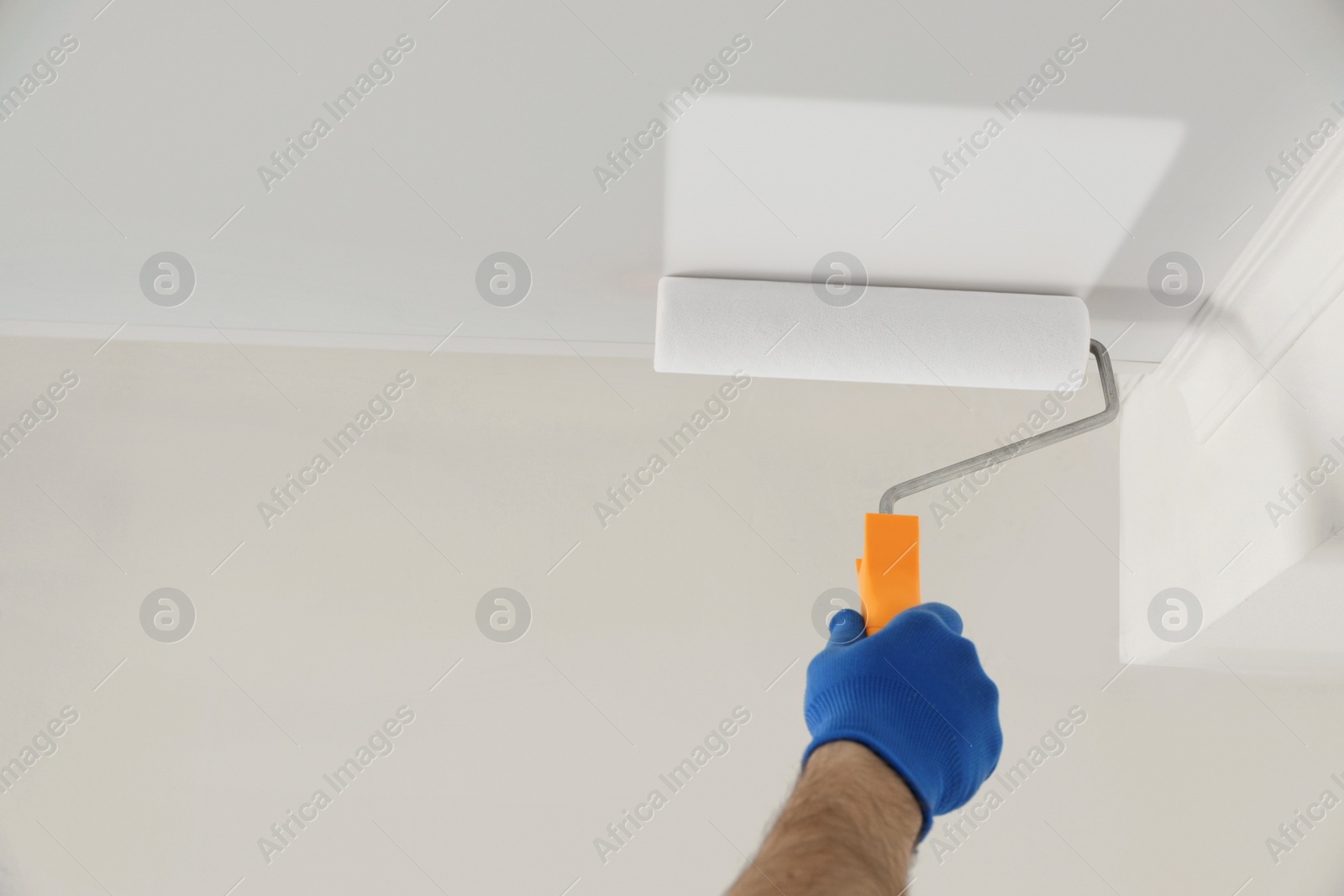 Photo of Handyman painting ceiling with white dye indoors, closeup. Space for text