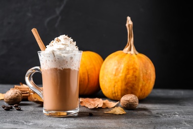 Pumpkin spice latte with whipped cream and cinnamon stick in glass cup on grey table