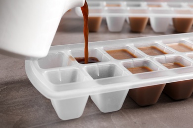 Photo of Pouring coffee in ice cube tray on table, closeup