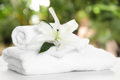 Soft bath towels and flower on table against blurred background