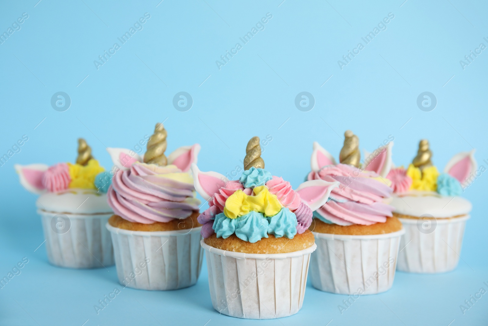 Photo of Many cute sweet unicorn cupcakes on light blue background