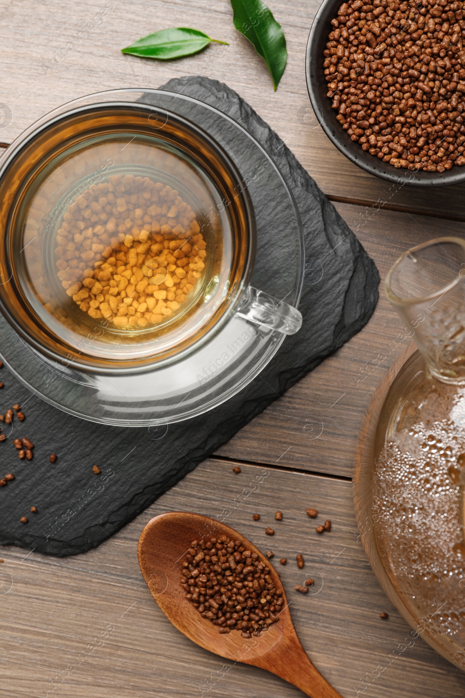 Photo of Cup of freshly made aromatic buckwheat tea and granules on wooden table, flat lay