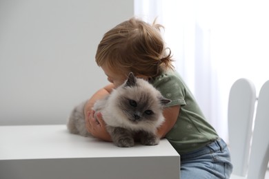 Photo of Cute little child with adorable pet at white table in room