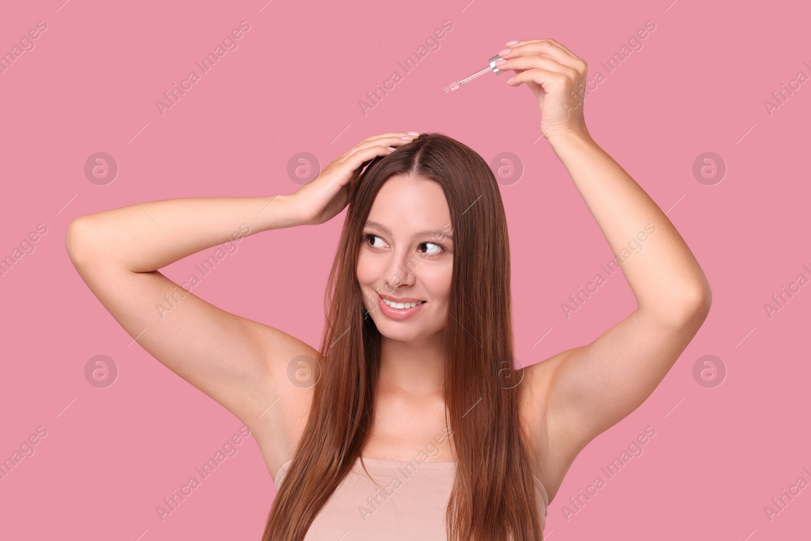 Photo of Beautiful woman applying serum onto hair on pink background