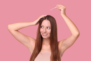 Beautiful woman applying serum onto hair on pink background