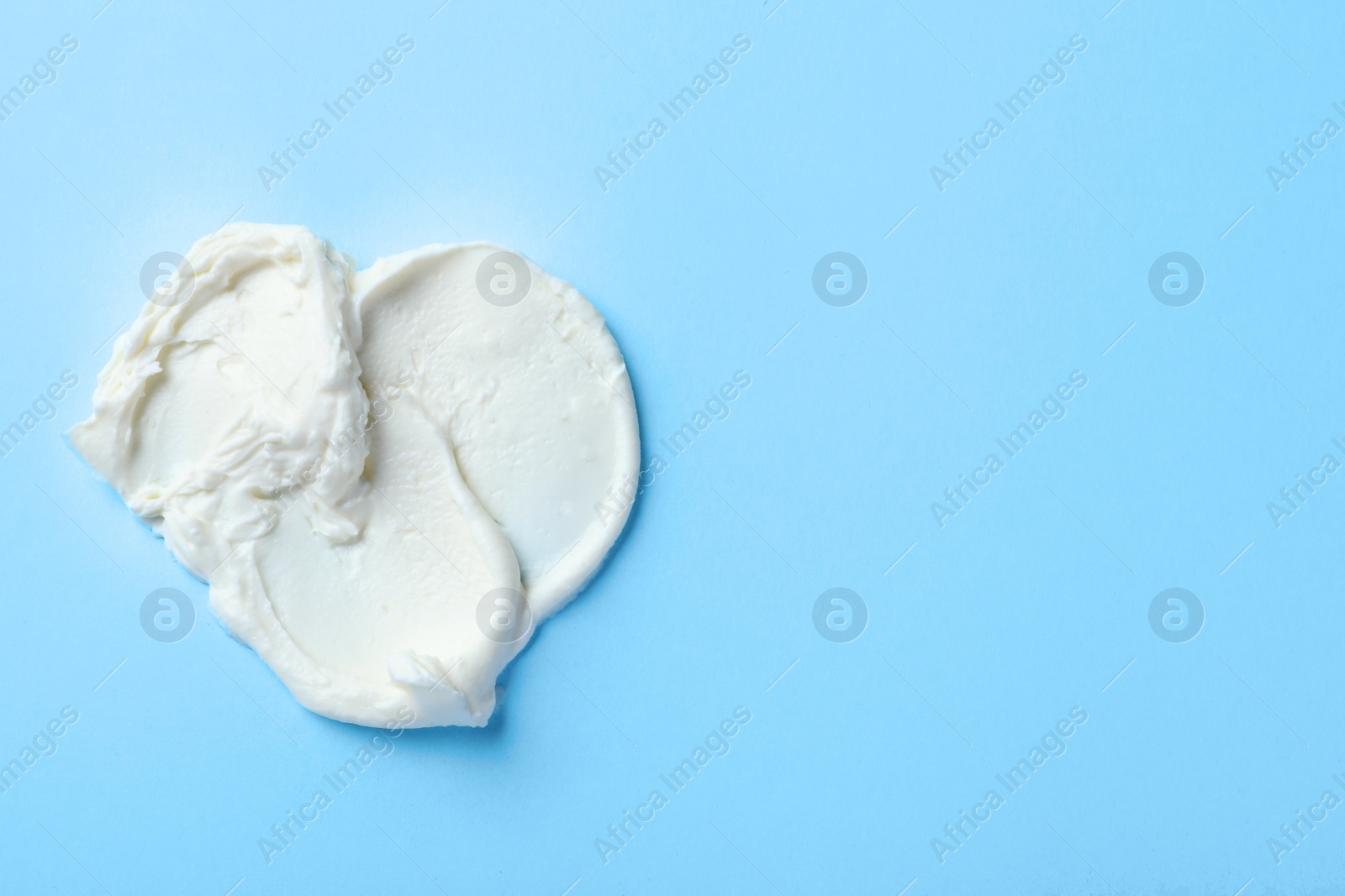 Photo of Smear of delicious cream cheese on light blue background, top view. Space for text