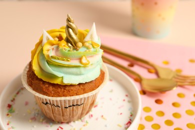 Photo of Plate with cute sweet unicorn cupcake on beige table, closeup. Space for text
