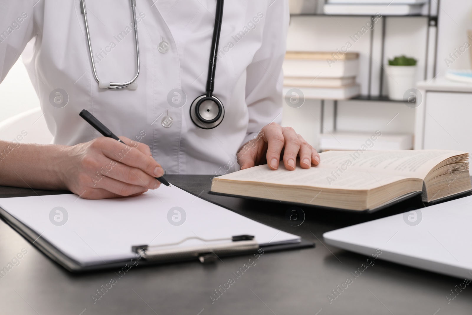 Photo of Medical student in uniform studying at table indoors, closeup