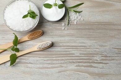 Photo of Toothbrushes, green herbs and sea salt on wooden table, flat lay. Space for text