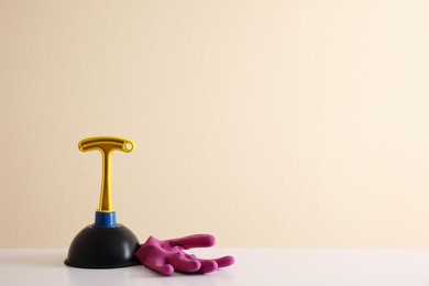 Photo of Plunger and rubber glove on white table against beige background. Space for text