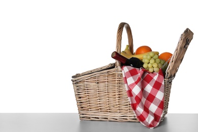 Wicker picnic basket with wine and different fruits on white background, space for text