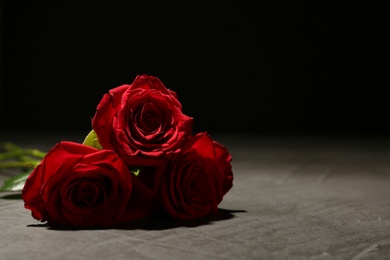 Photo of Beautiful red roses on table against black background. Funeral symbol