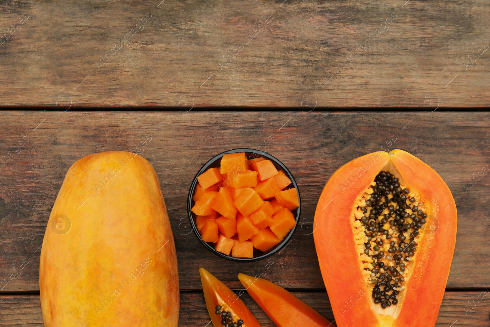 Photo of Tasty whole and cut papaya fruits on wooden table, flat lay. Space for text