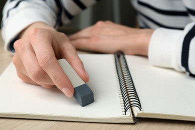 Photo of Woman erasing something in notebook at wooden table, closeup