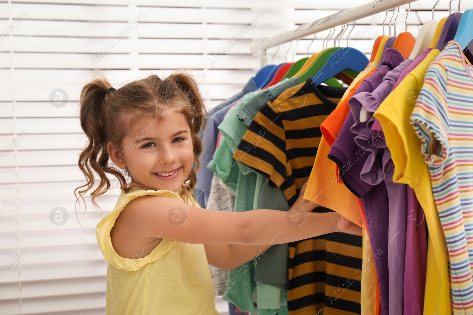 Photo of Little girl choosing clothes on rack indoors