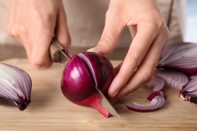 Photo of Young woman cutting ripe red onion on wooden board, closeup
