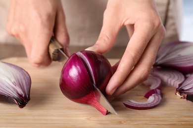 Young woman cutting ripe red onion on wooden board, closeup