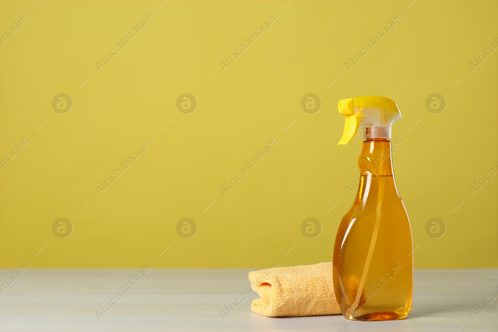 Photo of Bottle of cleaning product and microfiber cloth on light table. Space for text