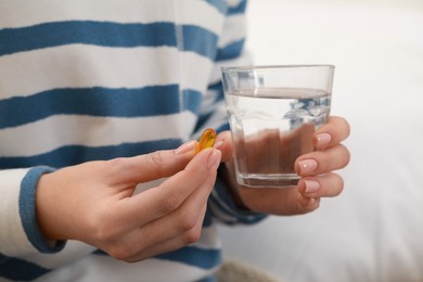 Photo of Woman holding glass of water and pill indoors, closeup