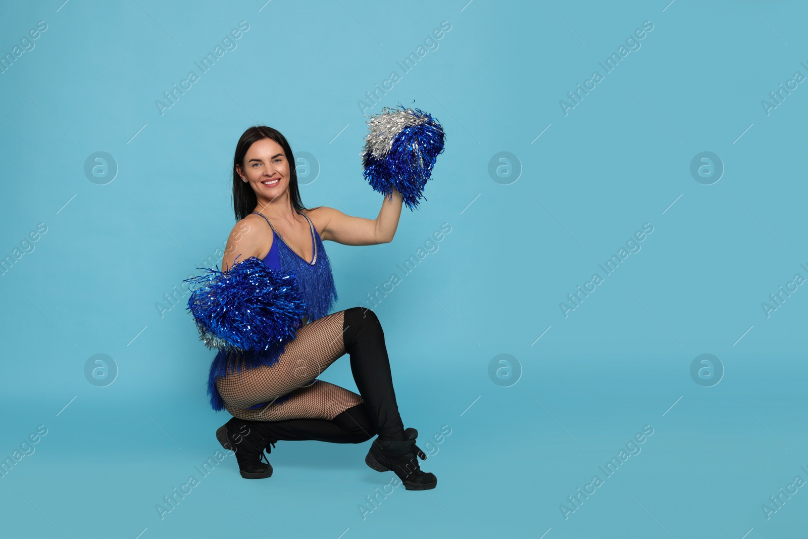 Photo of Beautiful cheerleader in costume holding pom poms on light blue background. Space for text