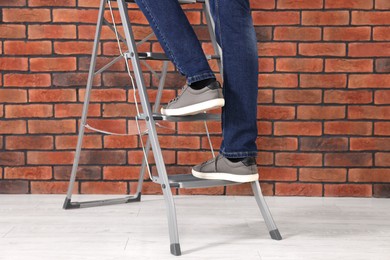 Photo of Man climbing up metal stepladder near brick wall, closeup