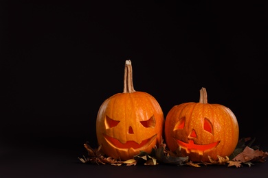 Photo of Pumpkin heads with autumn leaves on black background, space for text. Jack lantern - traditional Halloween decor