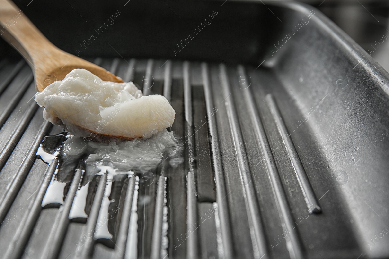 Photo of Wooden spoon with coconut oil in frying pan, closeup. Healthy cooking