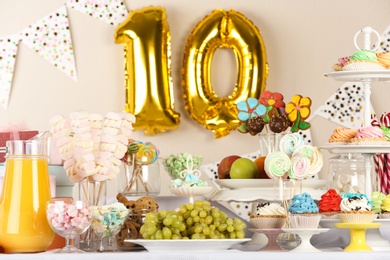 Photo of Golden number ten balloon over table with delicious treats at Birthday party indoors