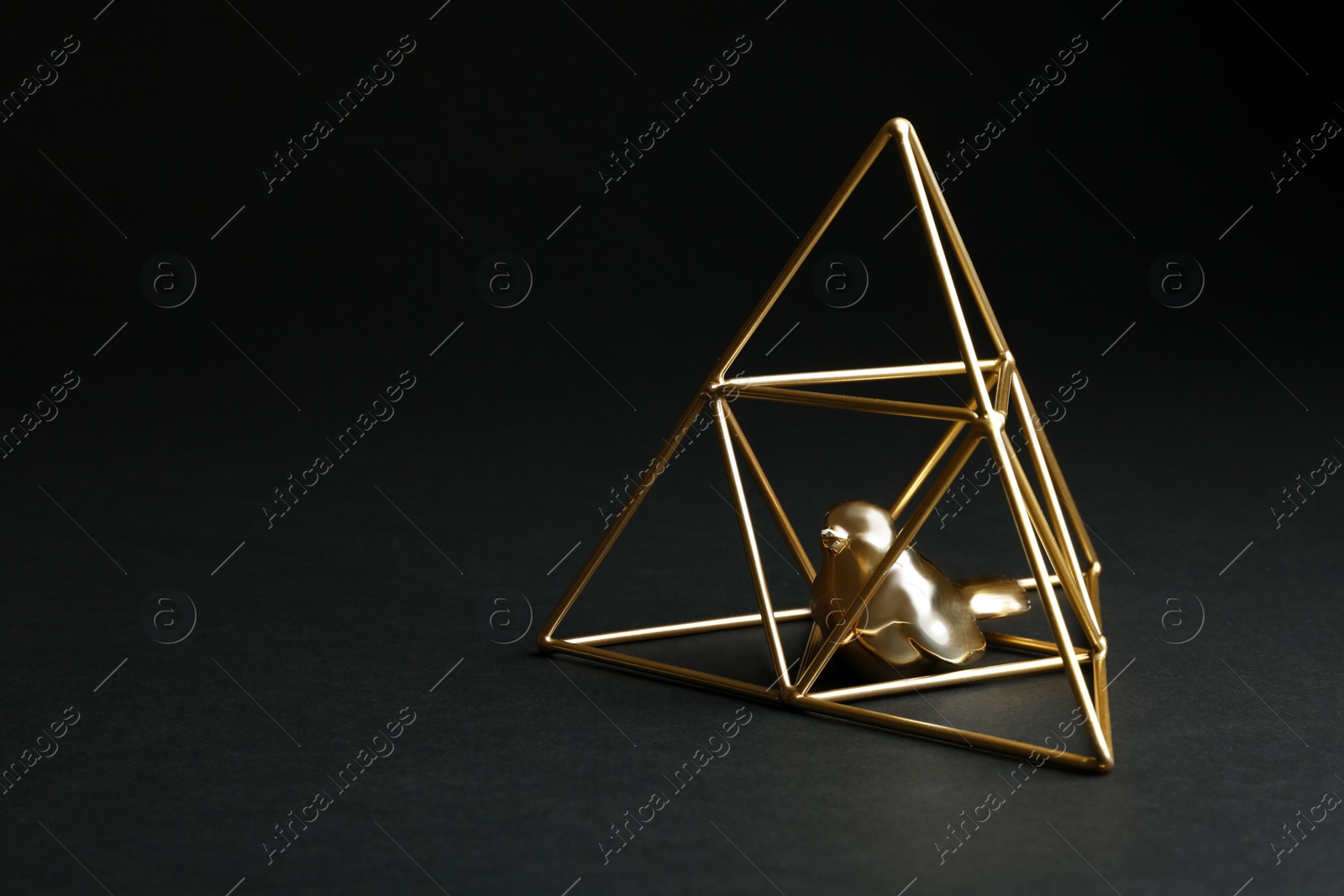 Photo of Decorative bird in gold pyramid on black background. Space for text