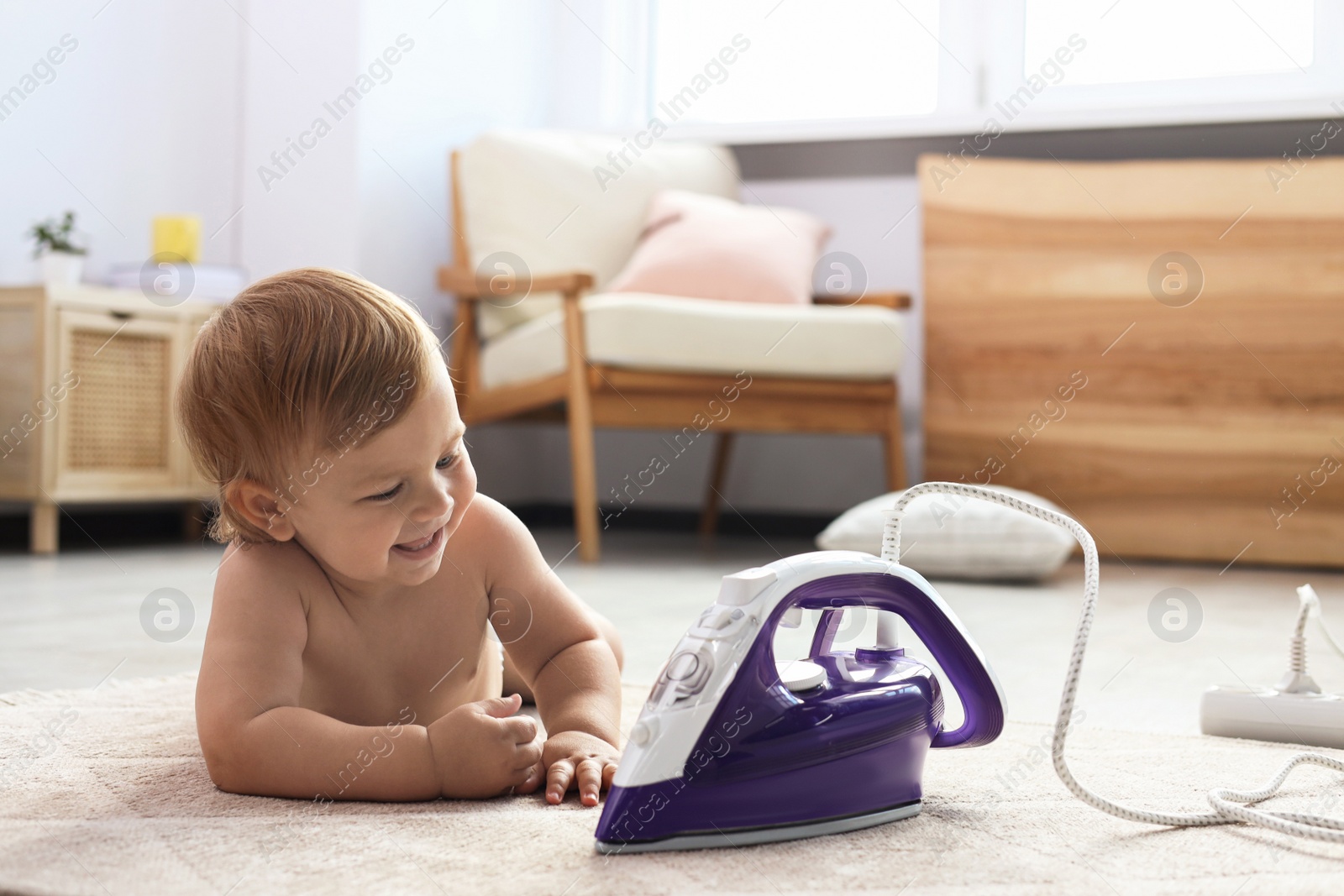 Photo of Cute baby playing with iron on floor at home. Dangerous situation