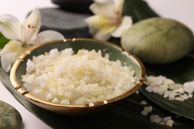 Photo of Aromatic sea salt, leaves and flowers on white table, closeup. Spa composition