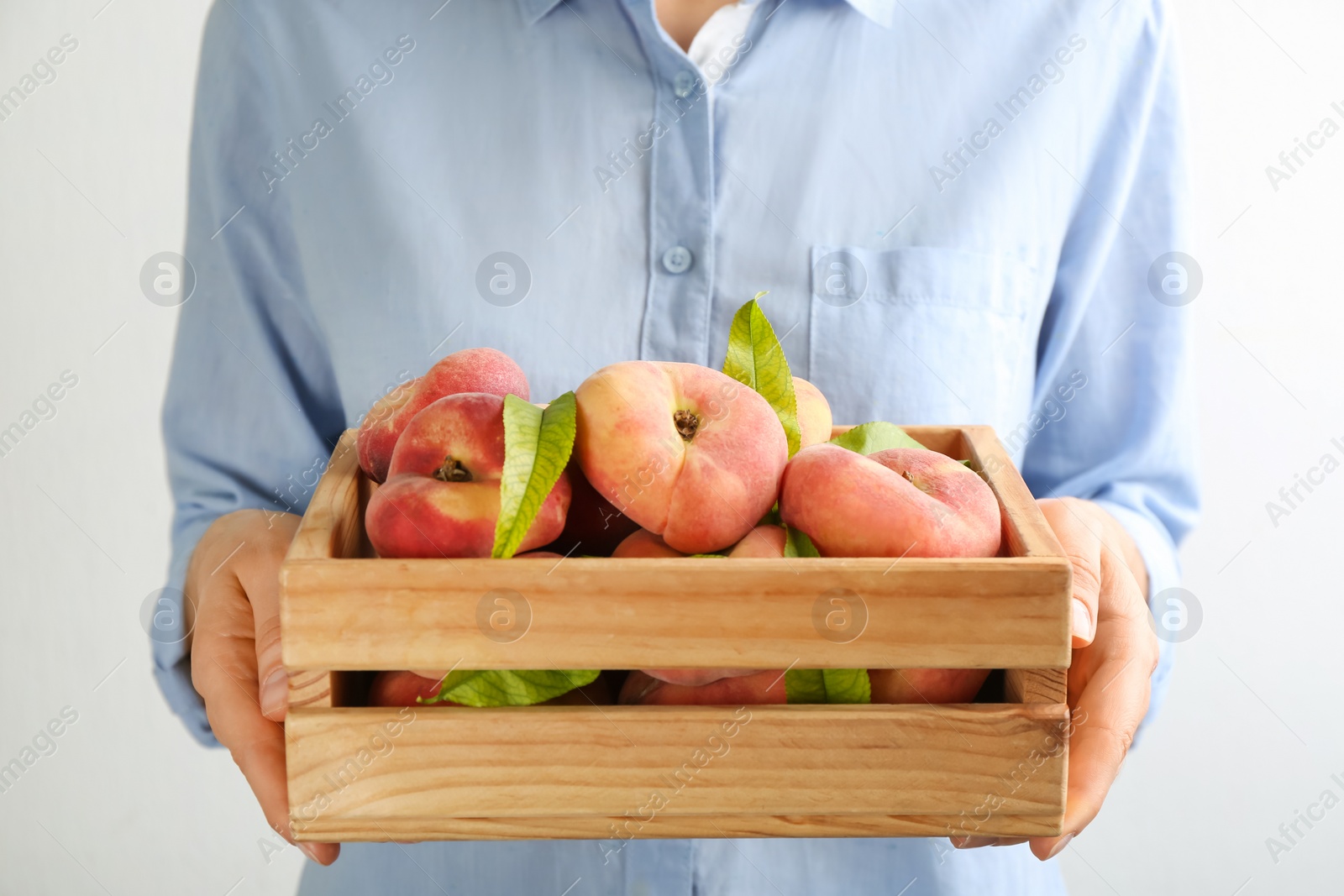 Photo of Woman holding wooden crate with fresh ripe donut peaches on light background, closeup