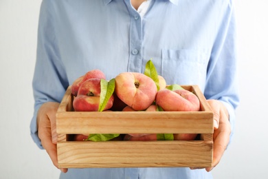 Woman holding wooden crate with fresh ripe donut peaches on light background, closeup