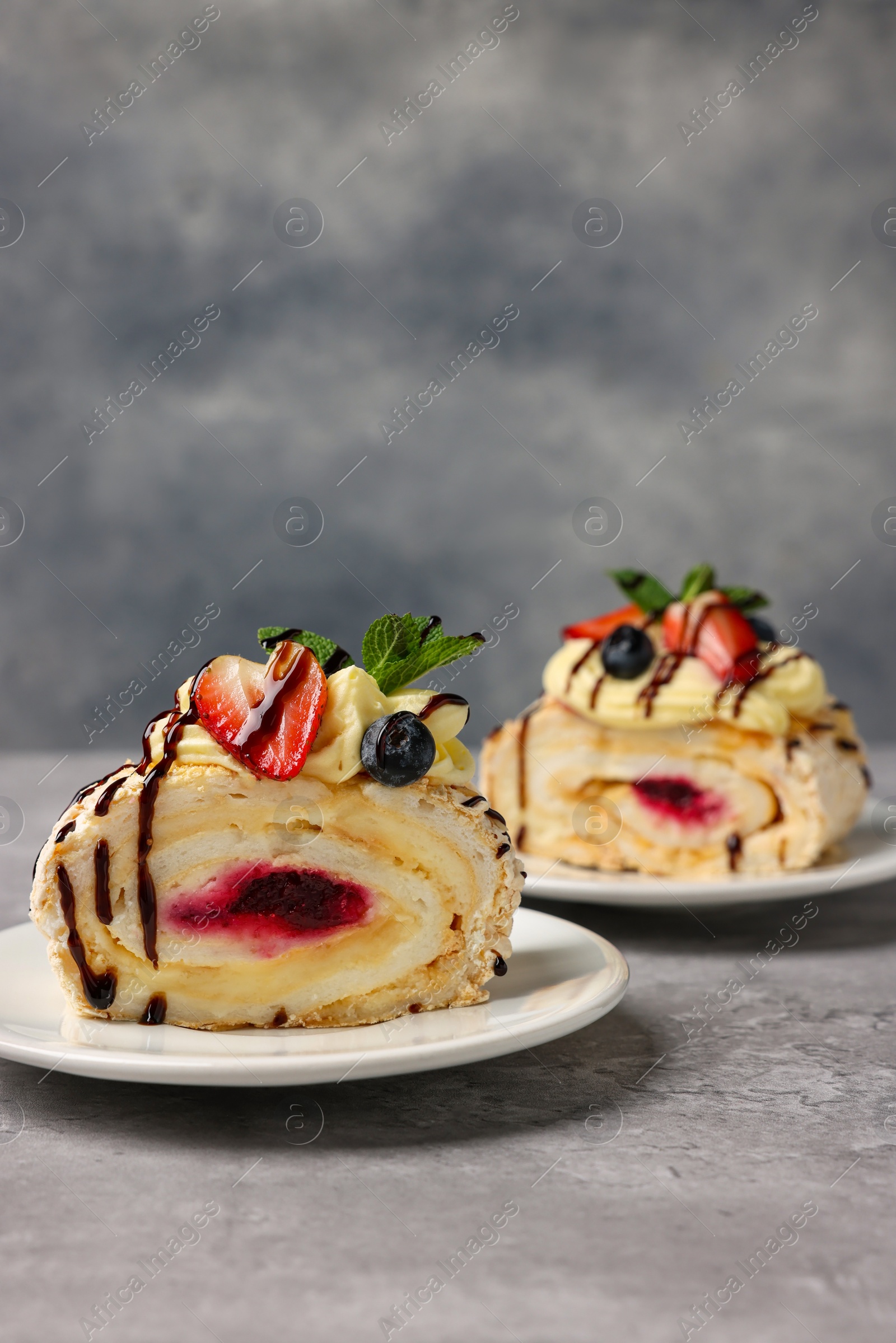 Photo of Pieces of tasty meringue roll with jam, cream, strawberry, blueberry and mint on light grey table